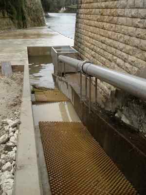 Canal avec une grille et un tuyau en métal au bord de l'eau.